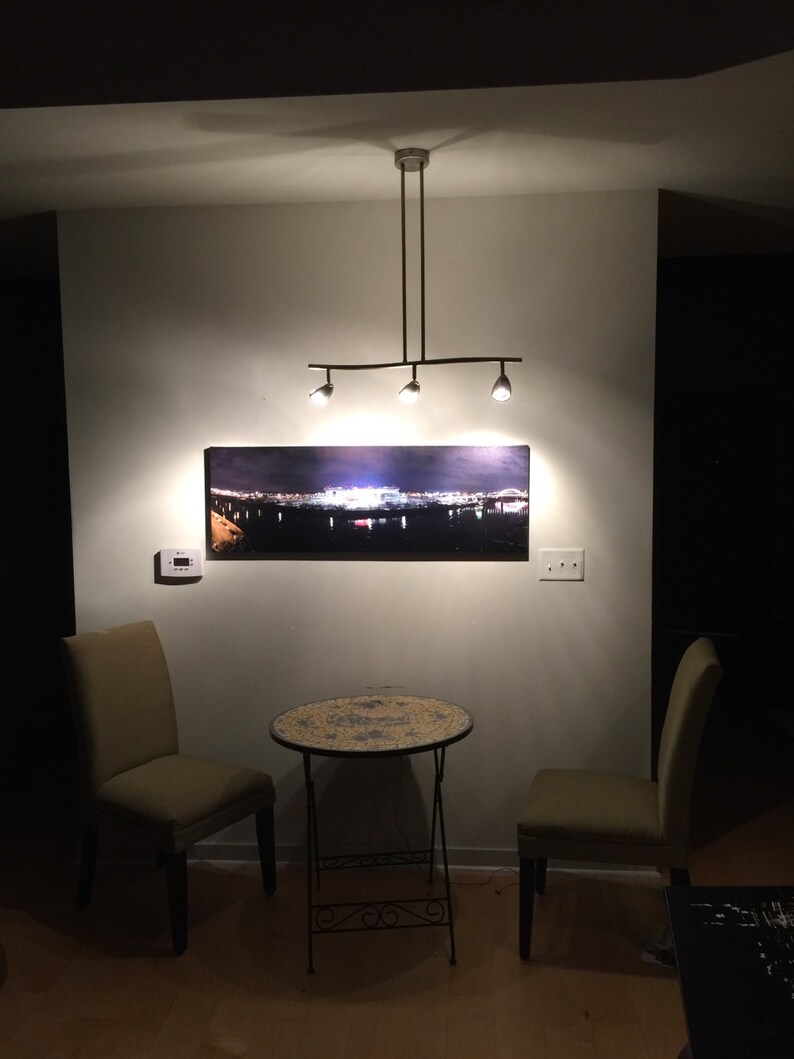 May include: Two chairs with a small round table in between them. The table has a mosaic tile top. The chairs are a light green color. A picture of a city skyline hangs on the wall above the table. A light fixture hangs from the ceiling.