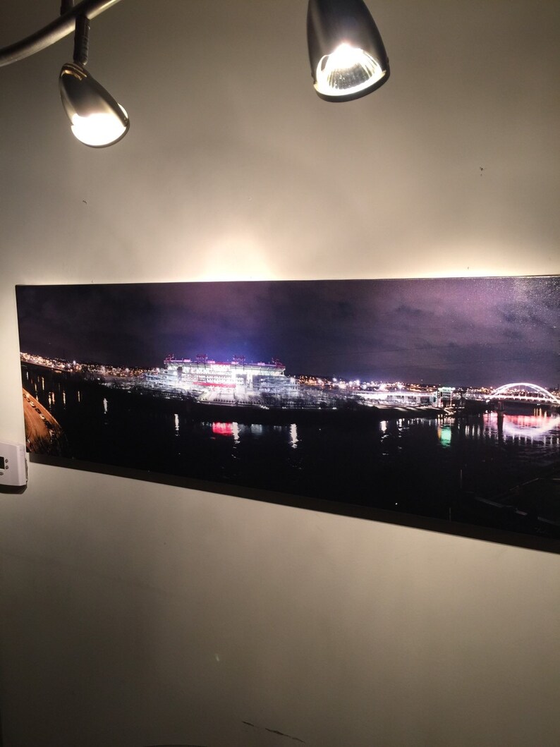 May include: A panoramic photograph of a city skyline at night, featuring a large stadium lit up with lights. The stadium is reflected in the water below, and there are several bridges in the distance.