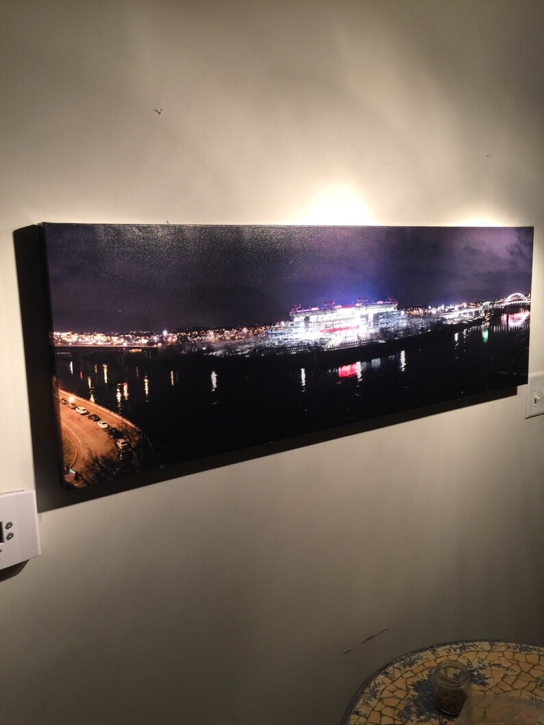 May include: A panoramic nighttime photograph of a city skyline with a large stadium lit up in the distance. The stadium is reflected in the water below. The city lights are visible in the background.