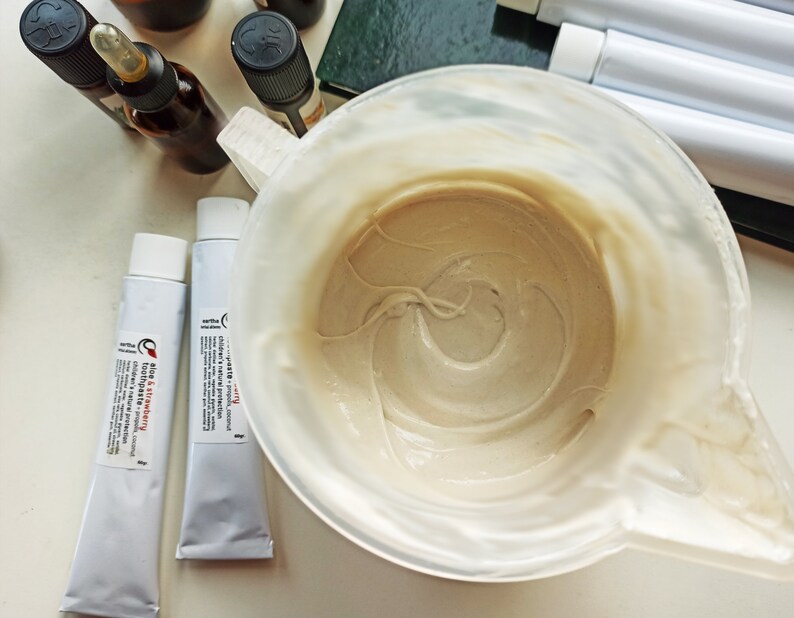 May include: Two white tubes of toothpaste with red and black text. The tubes are labeled "Clay & Strawberry Toothpaste" and "Charcoal + Propolis Coconut Toothpaste". A white bowl with a beige paste inside.