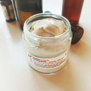 May include: A small glass jar of light brown toothpaste with a white label that reads "crystal turmeric toothpaste + propolis - aloe vera - prevention of gingivitis and plaque".