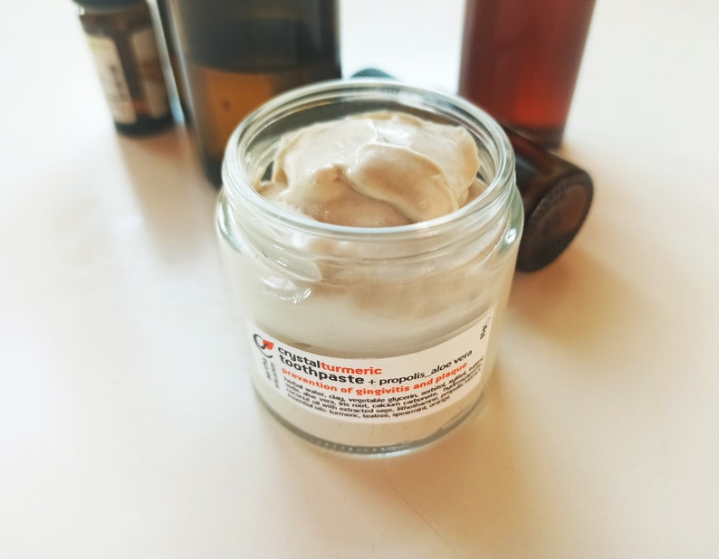 May include: A small glass jar of light brown toothpaste with a white label that reads "crystal turmeric toothpaste + propolis - aloe vera - prevention of gingivitis and plaque".