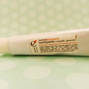 May include: A white tube of teatree & turmeric toothpaste with propolis and spearmint. The tube is labeled with the product name, ingredients, and benefits. The tube is 60 grams.