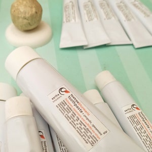 May include: Close-up of several white tubes of tea tree and turmeric toothpaste with propolis and spearmint. The tubes are labeled "eartha herbal alchemy" and have a list of ingredients and benefits.