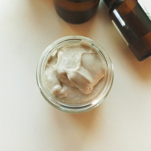 May include: A small glass jar filled with a light brown, creamy substance. The substance has a smooth, whipped texture.