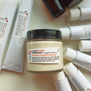 May include: A glass jar of crystal turmeric toothpaste with propolis and aloe vera. The jar is labeled with the text "crystalturmeric toothpaste + propolis aloe vera prevention of gingivitis and plaque".