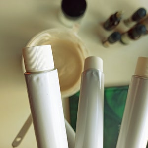 May include: Three white tubes with white caps, two of the tubes are partially visible, the third tube is fully visible. The tubes are on a green and white surface.