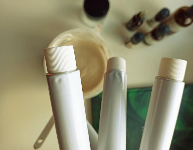 May include: Three white tubes with white caps, two of the tubes are partially visible, the third tube is fully visible. The tubes are on a green and white surface.