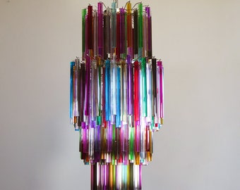 May include: A multi-tiered chandelier with a chrome chain and canopy. The chandelier features vertical glass rods in various colors, including red, purple, green, blue, and yellow. The light fixture hangs from the ceiling.