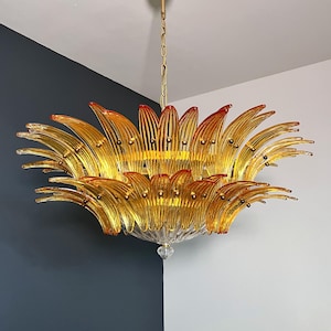 Pode incluir: Um grande candeeiro de cristal âmbar com uma corrente dourada e uma montagem de teto dourada. O candeeiro de cristal é feito de muitas peças de vidro curvadas que se assemelham a pétalas de flores.