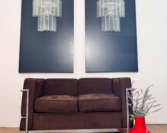 Peut inclure: Un canapé marron à deux places avec une structure chromée et un vase rouge avec des fleurs séchées. Deux lustres en verre assortis sont montés sur des panneaux bleu foncé au mur.