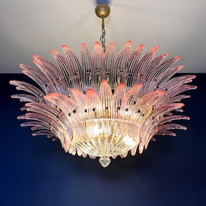 May include: A pink glass chandelier with a flower-like design. The chandelier has multiple layers of glass petals and a central light fixture.