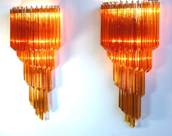 May include: Two amber glass wall sconces with cascading rectangular glass prisms. The sconces are lit and casting a warm glow.