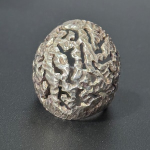 May include: A silver ring with a textured, organic design. The ring is made of a single piece of metal and has a unique, abstract shape.