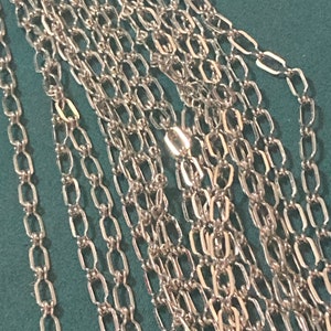 May include: A close-up of a silver chain with multiple strands. The chain is made of small, rectangular links.