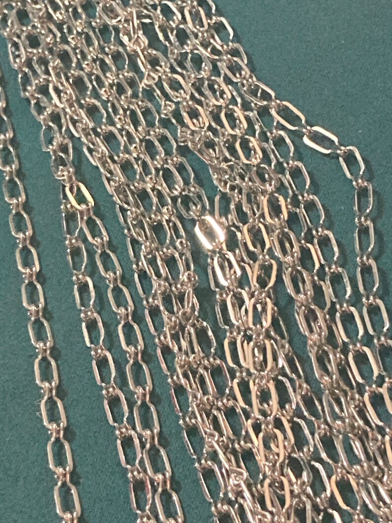 May include: A close-up of a silver chain with multiple strands. The chain is made of small, rectangular links.