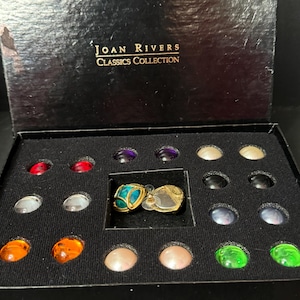 以下が含まれることがあります： 蓋に「JOAN RIVERS CLASSICS COLLECTION」と書かれた黒い箱。箱の中には、カラフルで丸い装飾的なイヤリングのセットが入っています。