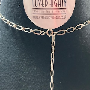 May include: A silver chain necklace with a silver clasp and a small silver pendant. The necklace is on a black background. The tag in the background says "Loved & Loved Again" vintage jewellery & collectables www.lovedandlovedagain.co.uk