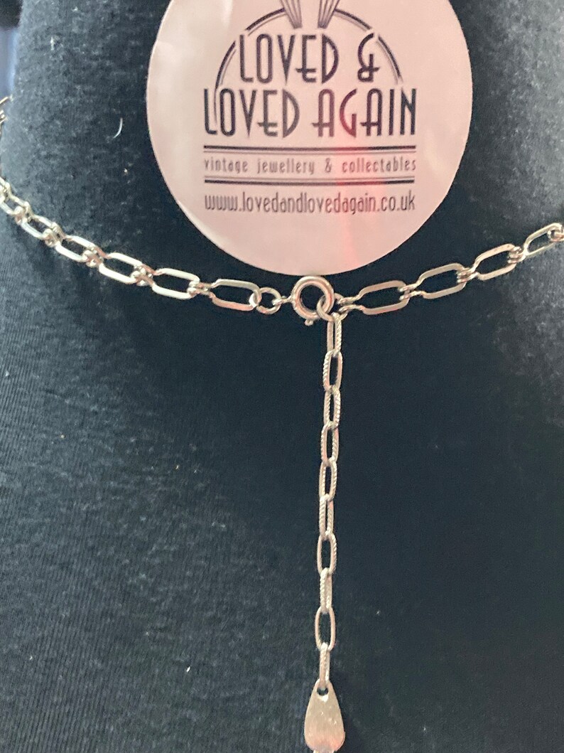 May include: A silver chain necklace with a silver clasp and a small silver pendant. The necklace is on a black background. The tag in the background says "Loved & Loved Again" vintage jewellery & collectables www.lovedandlovedagain.co.uk