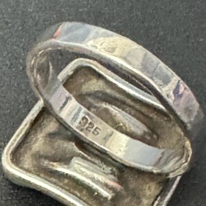 May include: Silver ring with a square-shaped design and the inscription "925" on the inside band.