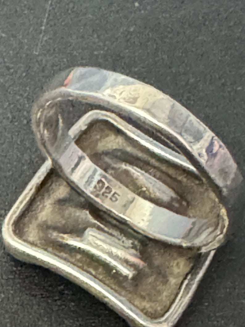 May include: Silver ring with a square-shaped design and the inscription "925" on the inside band.