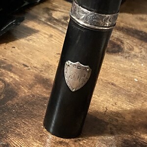 May include: A black cylindrical tube with a silver band and a silver shield with the initials "J.H." engraved on it.