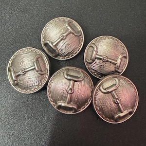 May include: Five silver-toned metal buttons with a raised design of a horse bit. The buttons are round and have a textured surface.