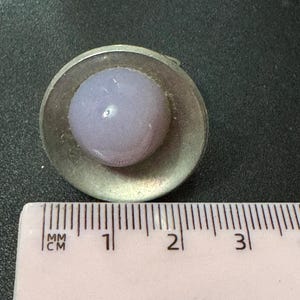 May include: A silver ring with a light purple glass cabochon set in a circular bezel. The ring is approximately 1 cm in diameter.