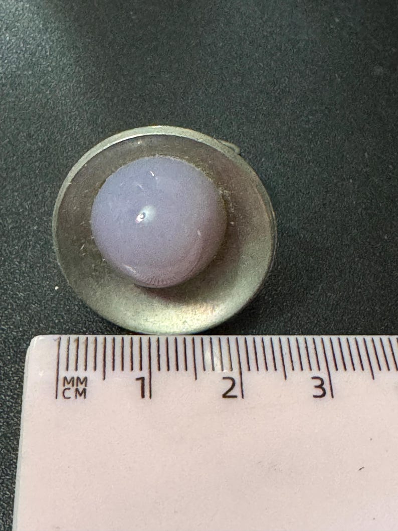 May include: A silver ring with a light purple glass cabochon set in a circular bezel. The ring is approximately 1 cm in diameter.