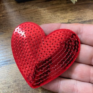 May include: Red heart-shaped sequin patch. The sequins are arranged in a pattern that creates a three-dimensional effect.