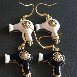 Puede incluir: Un par de pendientes de tono dorado con dise&ntilde;o de secador de pelo. Un par es negro con detalles blancos y el otro par es blanco con detalles dorados.