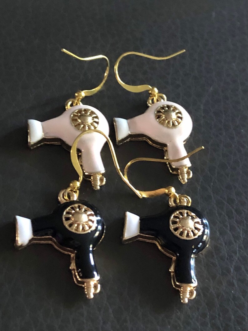 Puede incluir: Un par de pendientes de tono dorado con dise&ntilde;o de secador de pelo. Un par es negro con detalles blancos y el otro par es blanco con detalles dorados.