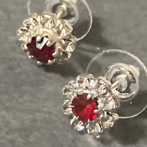 Puede incluir: Un par de pendientes de plata con una piedra roja rodeada de un halo de piedras transparentes m&aacute;s peque&ntilde;as.