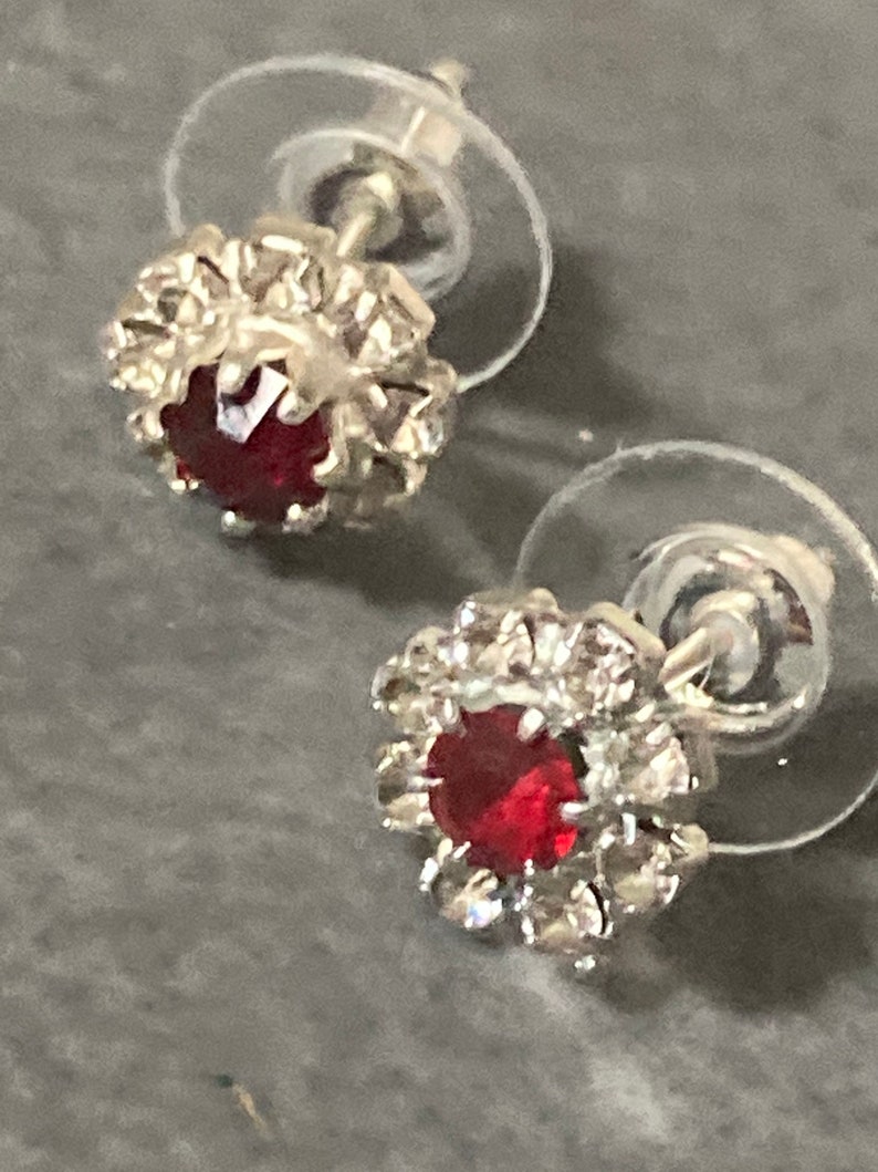 Puede incluir: Un par de pendientes de plata con una piedra roja rodeada de un halo de piedras transparentes m&aacute;s peque&ntilde;as.
