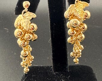 May include: A pair of gold dangle earrings featuring a grape cluster design with a leaf at the top.