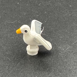 Peut inclure: Une figurine de mouette en plastique blanc avec un bec jaune et des marques noires sur les ailes. La figurine est perchée sur une base en plastique blanc.