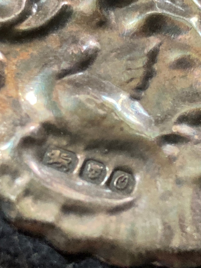 Puede incluir: Primer plano de un sello de plata con un le&oacute;n, una corona y una letra 'C'.