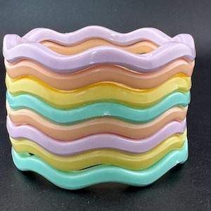 May include: A set of six wavy plastic bracelets in pastel colours, including light purple, peach, yellow, and light green.