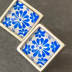 May include: A pair of silver stud earrings with blue and white floral patterns. The earrings are square shaped and have a silver metal frame.