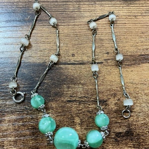 Pu&ograve; includere: Una collana a catena d'argento con una chiusura d'argento e perline di vetro verde. Le perline hanno un motivo a spirale e sono collegate da anelli d'argento.