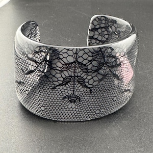 May include: A black and white lace design bangle bracelet. The bracelet is made of clear plastic and has a wide, flat design.