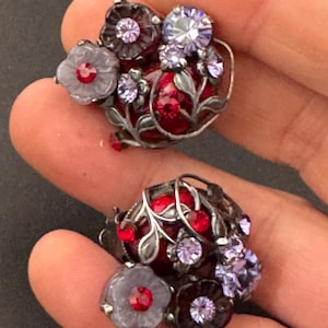 May include: A pair of silver tone earrings with a floral design. The earrings feature red, purple, and white flowers with rhinestones.