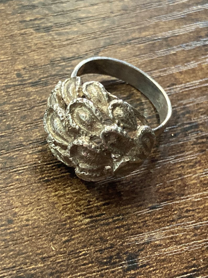 May include: A silver ring with a textured, floral design. The ring is made of metal and has a simple band.