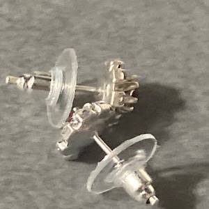 Puede incluir: Un par de pendientes de plata con una piedra roja en el centro. Los pendientes tienen un respaldo de pl&aacute;stico transparente.