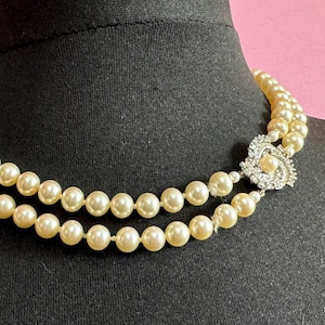 May include: A double strand pearl necklace with a silver and rhinestone clasp. The necklace is on a black mannequin.