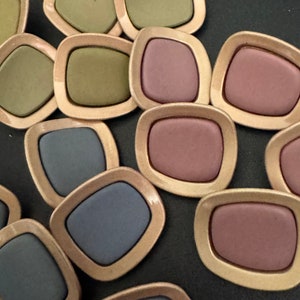 May include: A collection of 12 decorative, gold-rimmed, square-shaped buttons with a variety of colours, including green, pink, and blue.