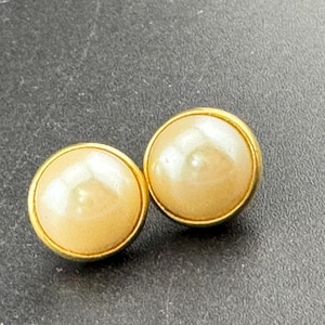 May include: A pair of round, cream-colored stud earrings with a gold-tone border. The earrings have a smooth, polished surface and a classic, elegant design. These earrings are suitable for everyday wear or special occasions.