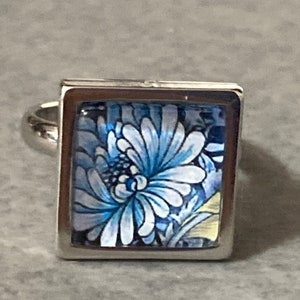 Könnte beinhalten: Ein silberner Ring mit einem quadratischen blauen und weißen Blumendesign.