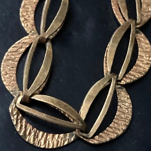 May include: Gold-toned metal chain necklace with a unique, interlocking oval link design. Each link has a textured surface.