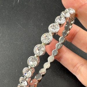 May include: A silver bracelet featuring clear, round gemstones. The gemstones are set in individual bezels. The bracelet has a scalloped edge design. The bracelet is shown against a dark background.
